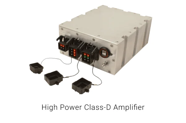 A square metallic box with three sets of electrical ports on one side that are connected to black caps with string. There is a white background and text that says "High Power Class-D Amplifier".