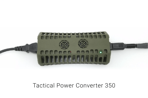 A green TPC plugged in on both of its ends. There is a small green light emitting from its corner to indicate that the device is on. The device is shown to have various vents and is rectangular in shape. There is a white background and text saying "Tactical Power Converter 350"